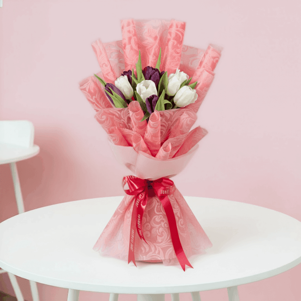 Purple and white tulips in a pink tissue wrap with greenery and tied with a pink ribbon.
