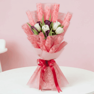 Purple and white tulips in a pink tissue wrap with greenery and tied with a pink ribbon.