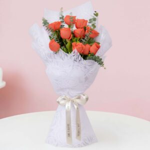 A bouquet of vibrant mix of orange roses and fresh eucalyptus branches, expertly wrapped in a white non-woven paper and finished with a satin ribbon.