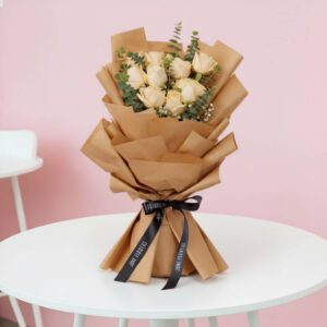 A vibrant bouquet of peach roses is complemented by fresh eucalyptus.The arrangement is wrapped in rustic brown non-woven paper and finished with a sleek black satin ribbon.