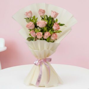 Soft pink roses with fresh green leaves are elegantly wrapped in off-white paper and tied with a vibrant pink ribbon.