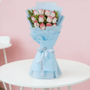 Bouquet of 12 pink roses with green leaves wrapped in non-woven paper and finished with white ribbon.