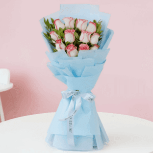 Bouquet of 12 pink roses with green leaves wrapped in non-woven paper and finished with white ribbon.