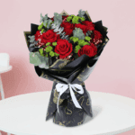 A bouquet of red roses with green fillers in a black korean wrap, finished with a “Love You” topper and ribbon.