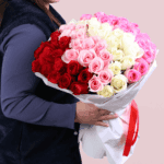 A bouquet of red, pink, and white roses in an elegant white wrap, finished with a red ribbon.