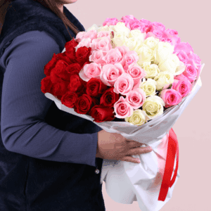 A bouquet of red, pink, and white roses in an elegant white wrap, finished with a red ribbon.