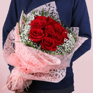 A bouquet featuring red roses with white baby’s breath in a pink Valentine wrap, finished with a “Love You” message topper.