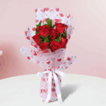 Red roses bouquet with green fillers in a heart-print wrap, finished with a white ribbon.